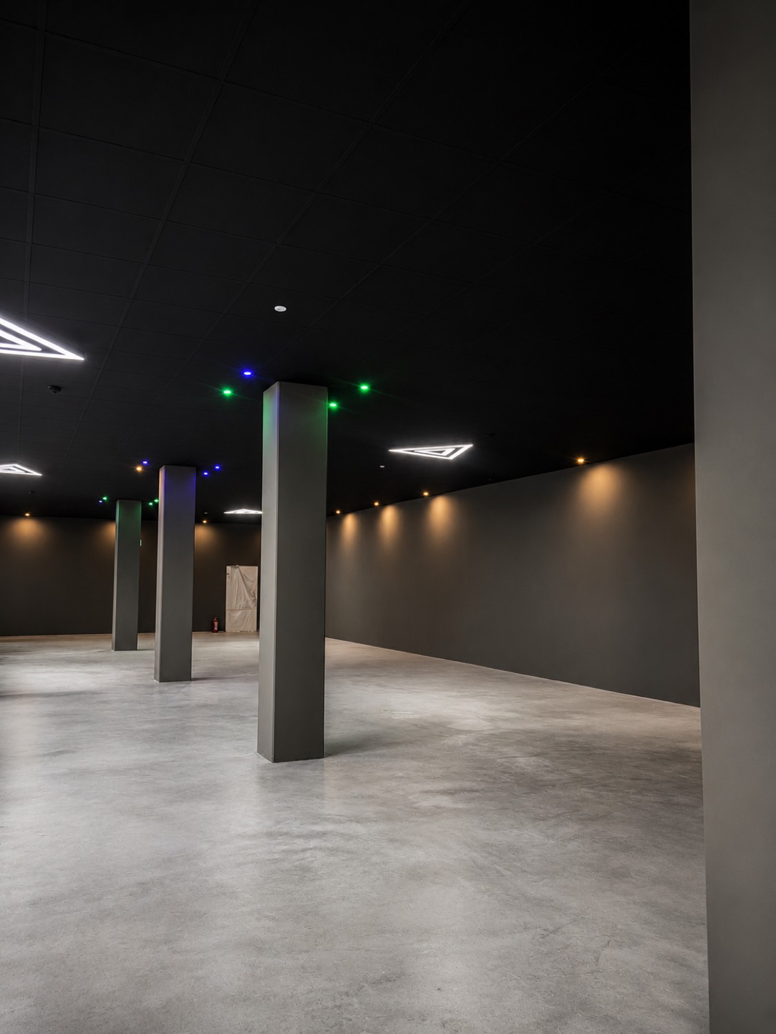 Fertig ausgebaute dunkle Gewerbefläche mit Säulen und markanter Lichtplanung